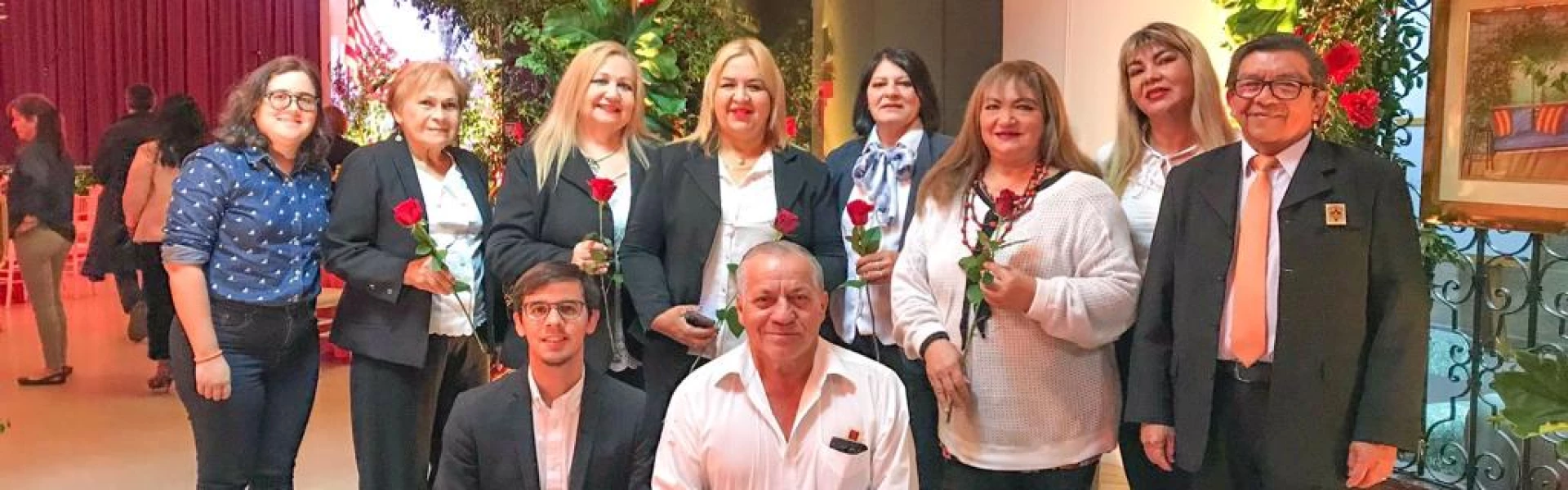 Un grupo de gente, 2 agachados y 8 parados, sosteniendo rosas rojas